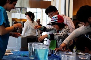Kids and adults dip strands of string into buckets of blue coloured water