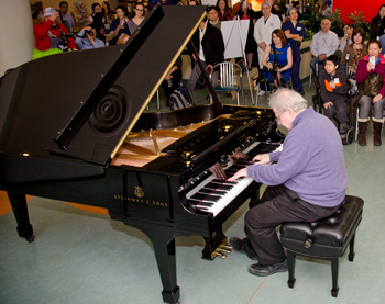 A man plays a grand piano with an audience of children and adults watching him