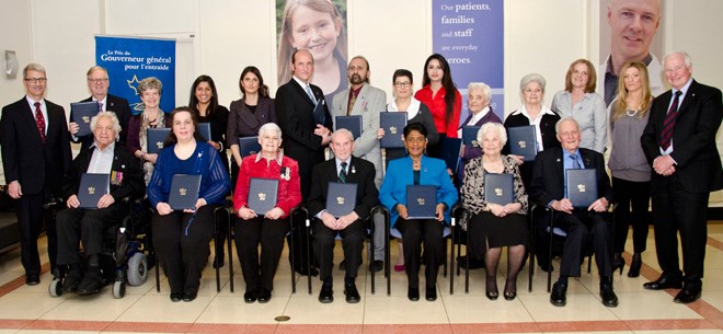 A large group of adults gather together standing and in chairs. Many of the adults are holding navy blue and gold folders.