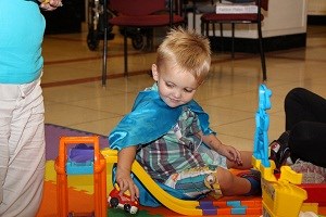 Boy wearing cape plays with toy cars.