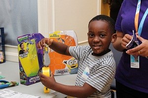 Child looks at camera while playing with a toy. Toy packaging is on the table behind the child.