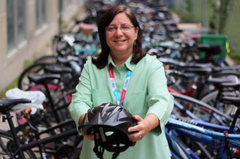 A woman holds out a helmet in front of a large bike rack full of bikes 