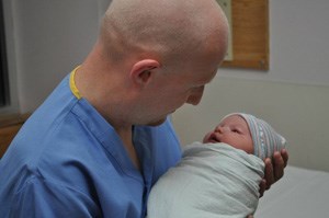 A man in scrubs holds a small baby bundled in a blanket