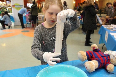 A young girl wearing latex gloves dips a piece of plaster bandage into a bowl of water