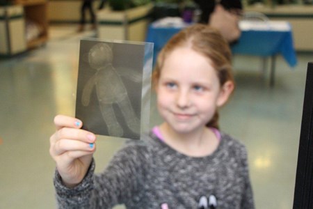 A young girl holds up an xray image of a stuffed teddy bear