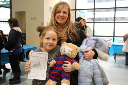 A young girl and mom hold a teddy bear and teddy bear clinic pamphlet