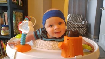 Baby wearing a headband in an exersaucer.