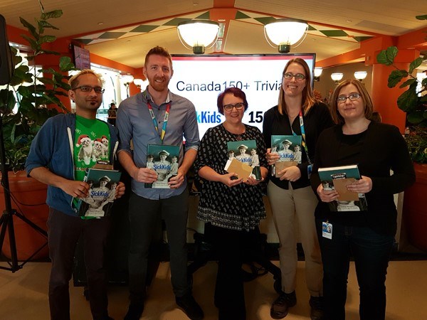Group of five adults stand together, each holding a copy of a SickKids book.