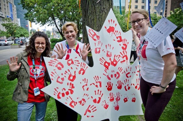 Staff stand around a white maple leaf with red handprints painted on it.