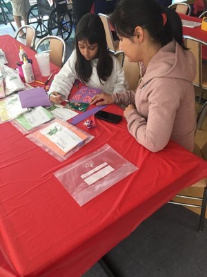Two people sit at a table doing a craft.