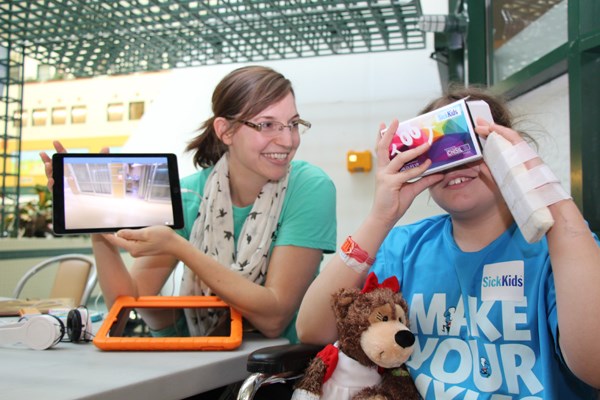 Child looks into virtual reality viewer. Woman holds tablet showing a video tour.