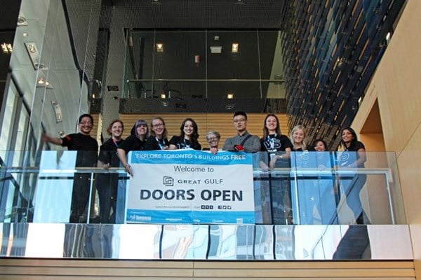 Group stands behind a glass balcony with a Doors Open sign.