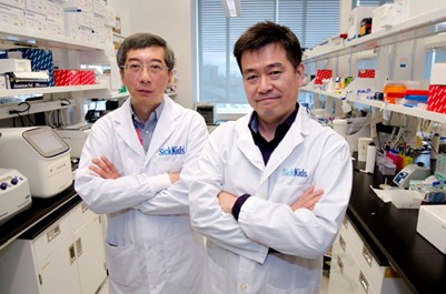 Two men stand side by side in a lab wearing lab coats.