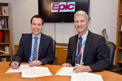 Two men sign papers while seated at a table.