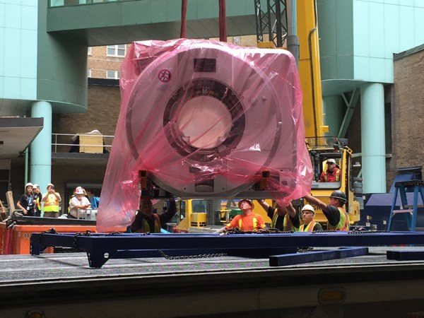 MRI machine wrapped in plastic and being lifted off of truck.