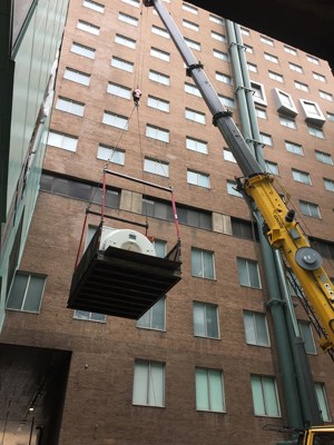 MRI machine hangs from a crane in front of a brick building.