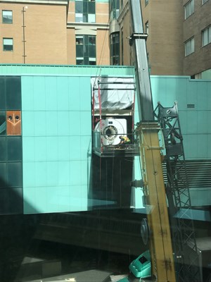 MRI hangs in front of a hole in the wall of the building, suspended by a crane.