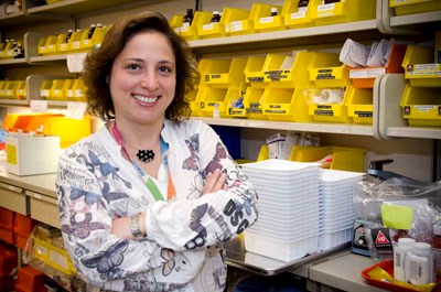 Woman stands in front of lab bench and stocked shelves.