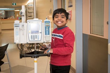 Young boy stands in hallway with IV pump.