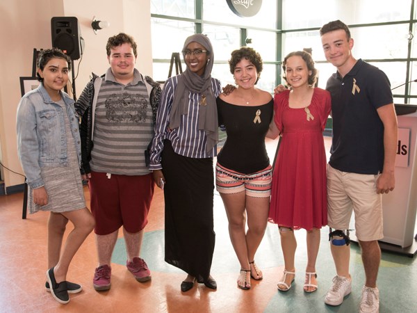 Group of six teens stand arm-in-arm.