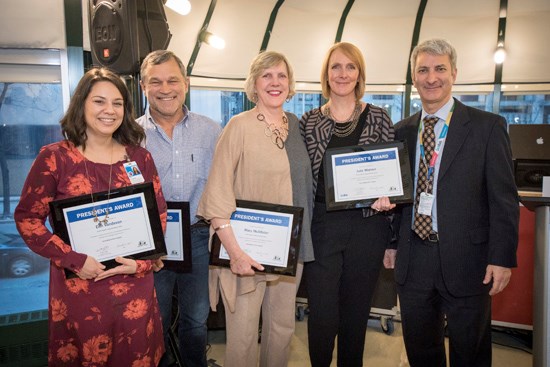 Five staff stand together, four holding award plaques.