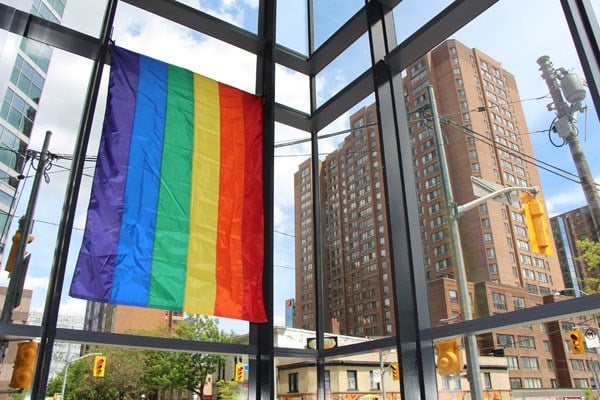 Rainbow flag hangs vertically inside a corner window.