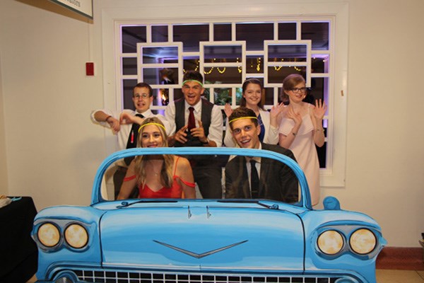Teens pose together behind a cutout of a vintage car.