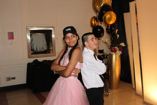 Teen boy and girl stand back to back, each with their arms crossed.