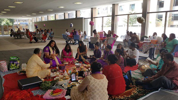 A large group sit together at a table close to the floor, with several tables behind them.