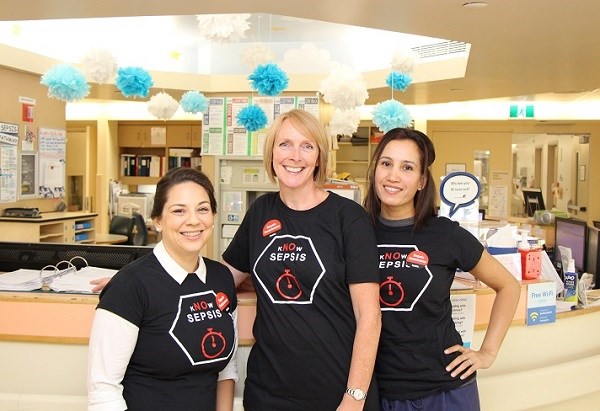Three women stand together wearing shirts that read "kNOw" sepsis.