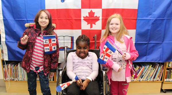 Three girls pose in front of a SickKids flag.