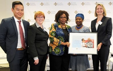 Group of five people stand together, two hold a framed certificate.