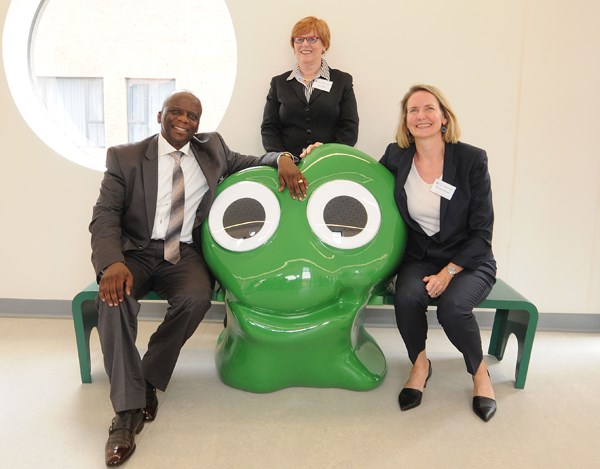 Three people pose around a frog-like sculpture.