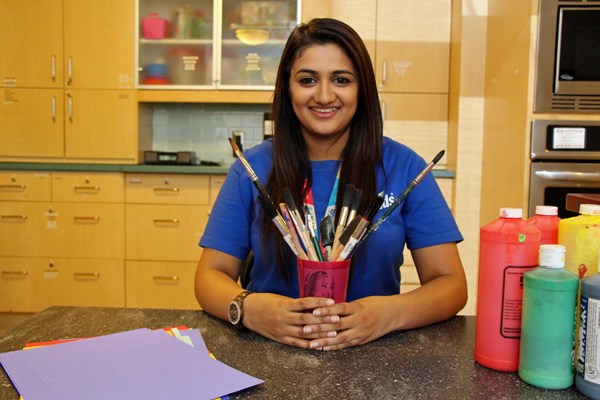 Young adult poses holding a cup of paintbrushes.