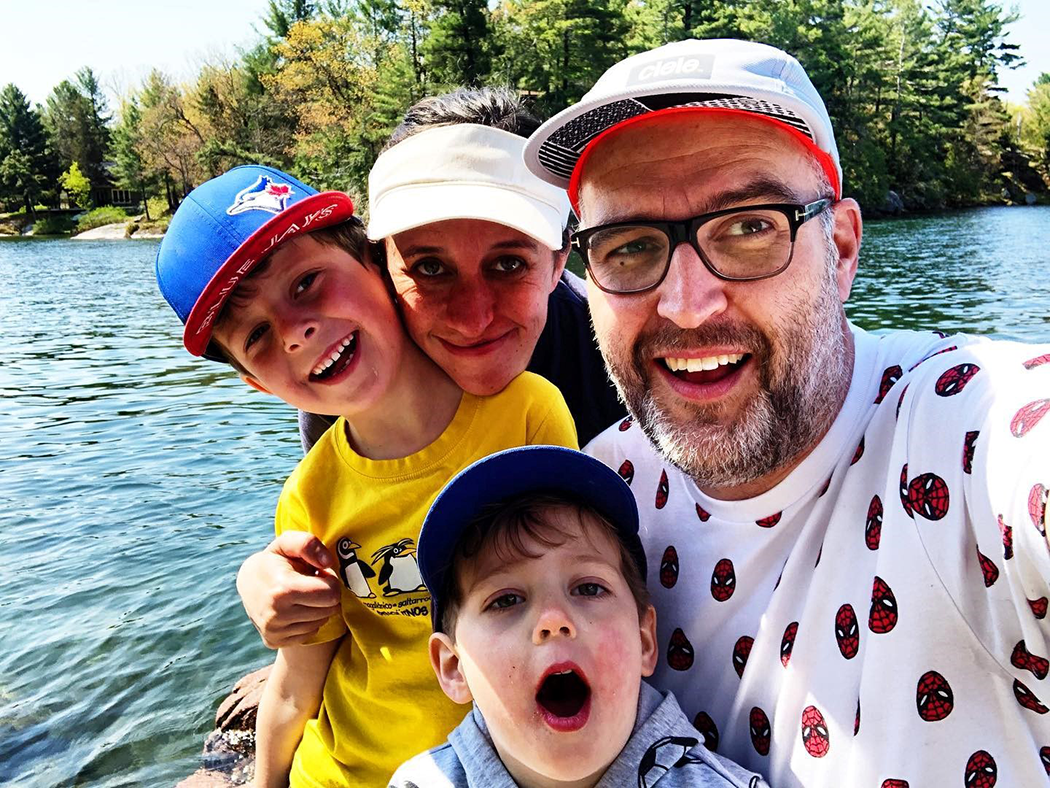 Two kids and two adults huddle together smiling in front of a scenic lake and shoreline