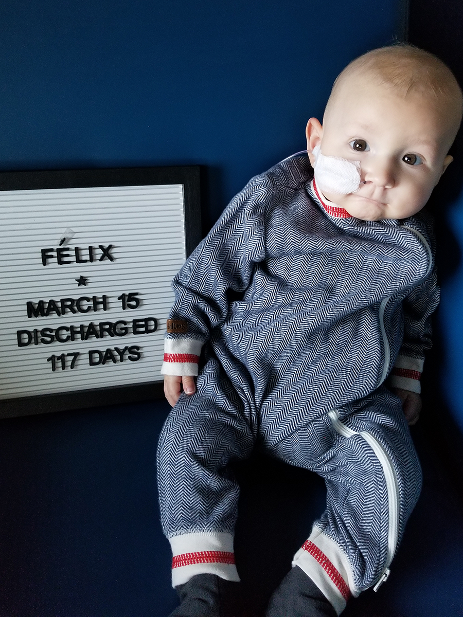A young baby sits up next to a letterboard sign that says Felix March 15 Discharged 117 days