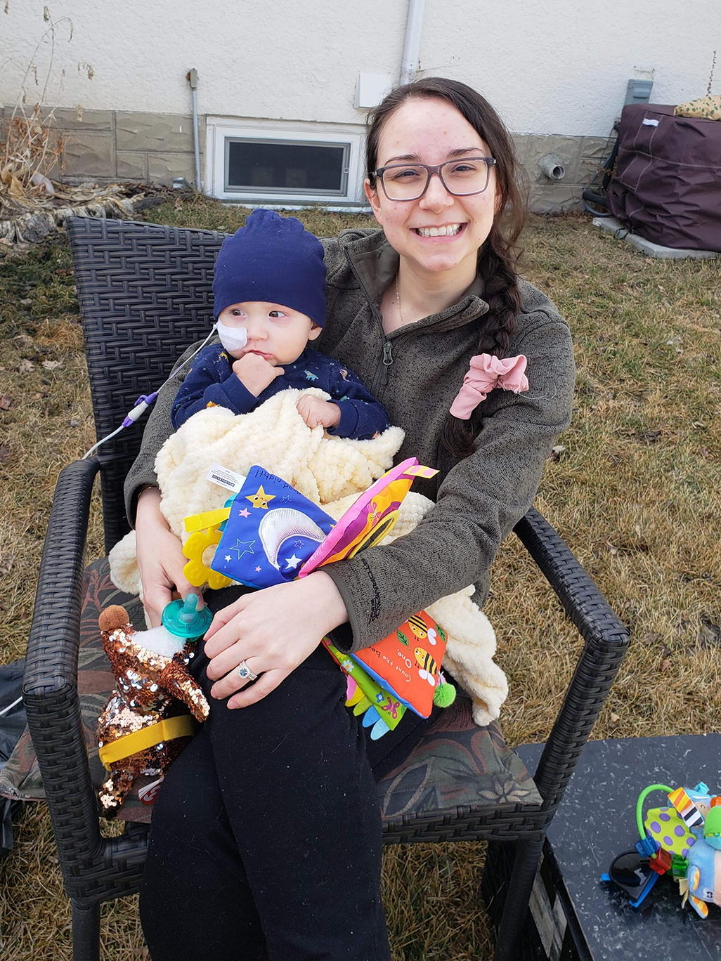 A smiling woman with a baby on her lap sits outside on a lawn chair