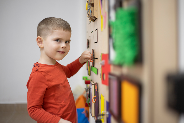 Young boy looks at the camera as he plays with a colourful wooden puzzle