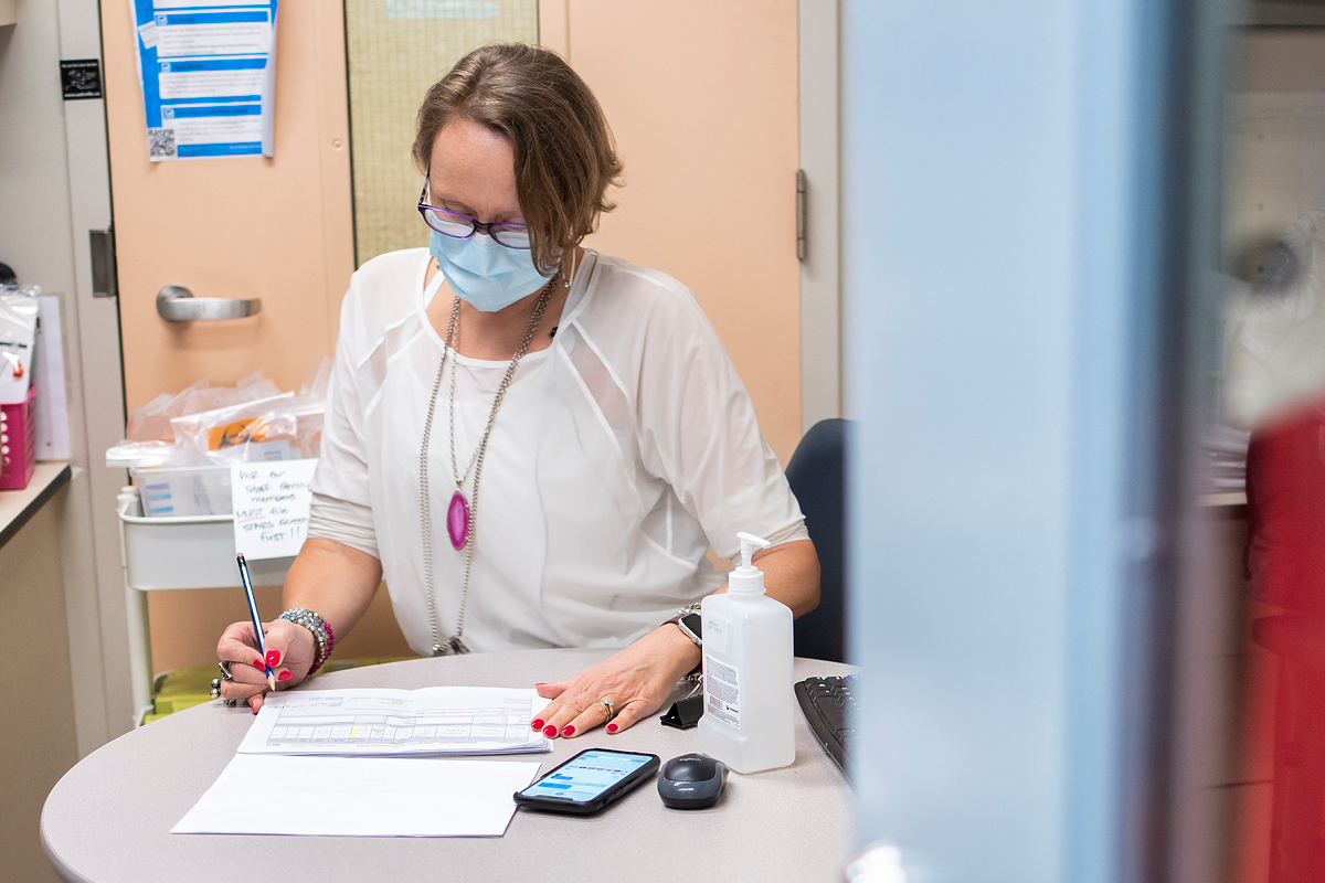 Person seated at a desk reviewing paperwork, wearing a mask.