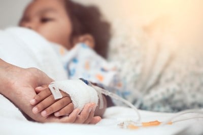 An adult's hand holding onto a child's hand that is connected to an IV.