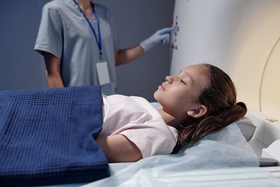 Child lays on bed of CT machine.