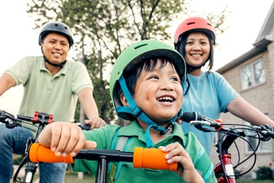 A man, girl and young boy ride bicycles and scooters. They all wear helmets.