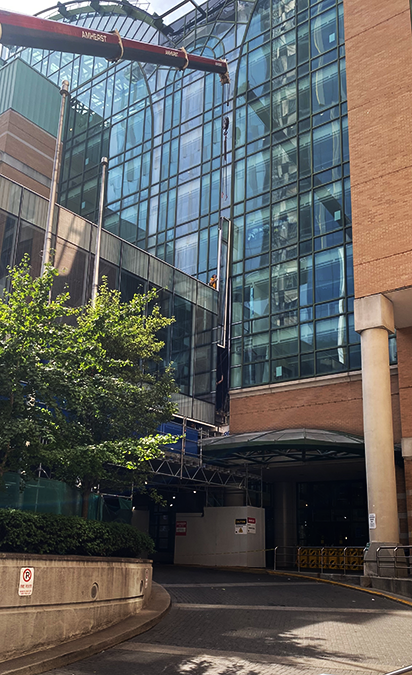 A construction crane lifts a thin panel of glass into an opening next to other panels of glass