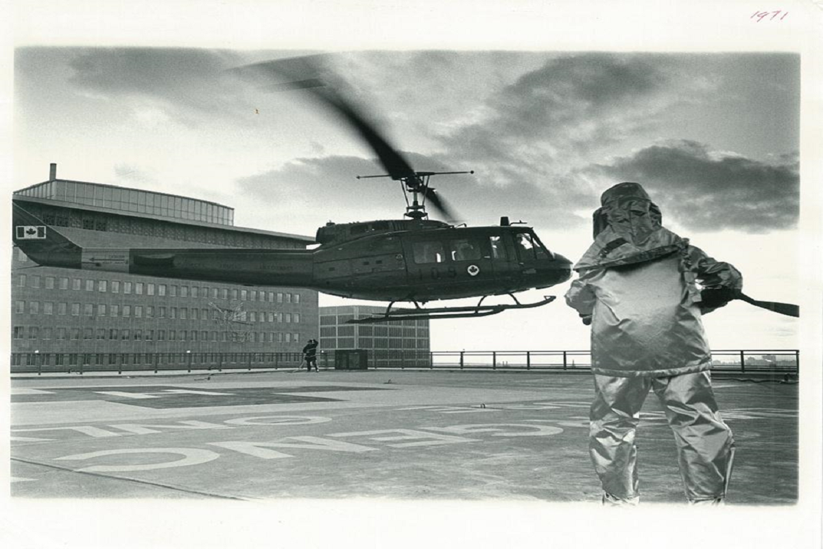 Black and white image showing a firefighter holding a hose as a helicopter hovers.