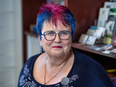 Person with colourful hair and wearing glasses smiles to the camera.