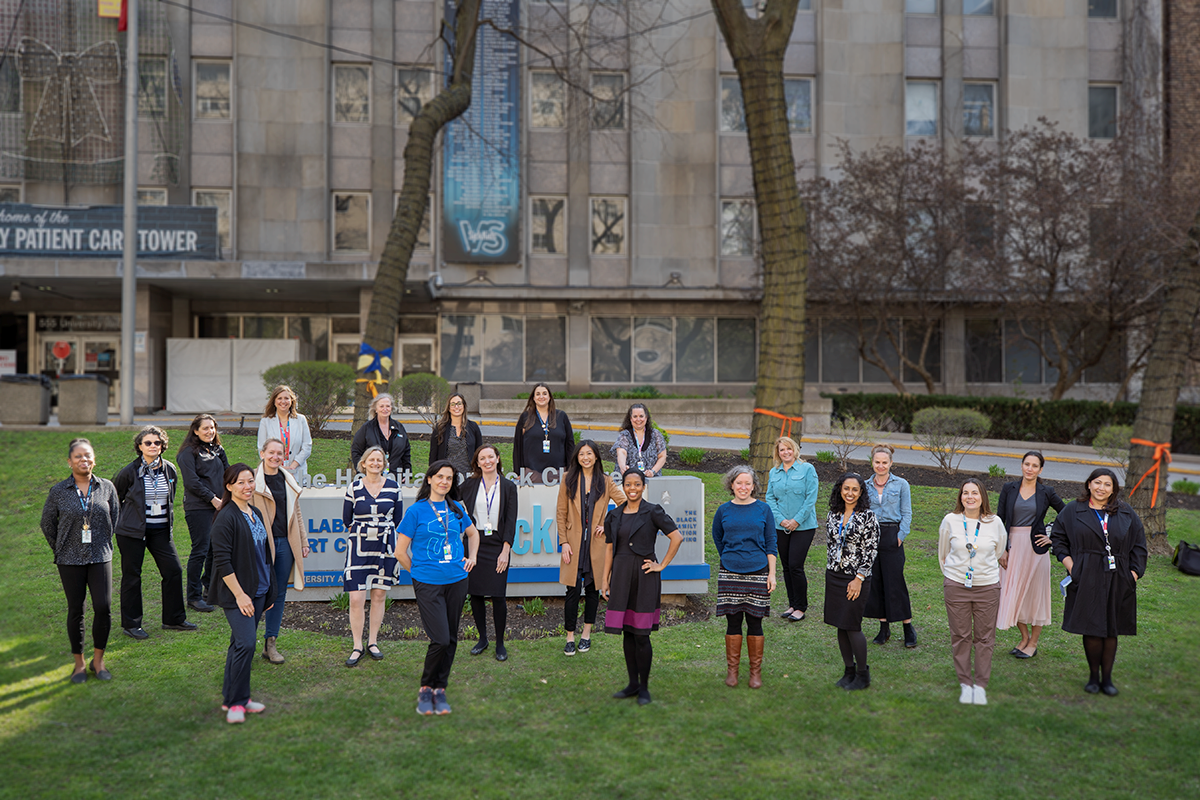 Twenty two women stand together outside SickKids University Ave. side.