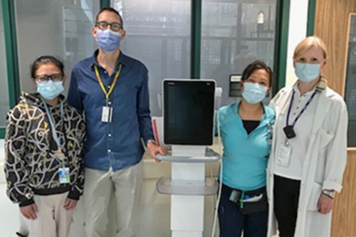 Four staff stand together wearing masks, with a piece of clinical equipment.