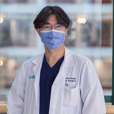 Headshot of surgeon Osami Honjo. He wears a surgical mask, glasses and white lab coat.