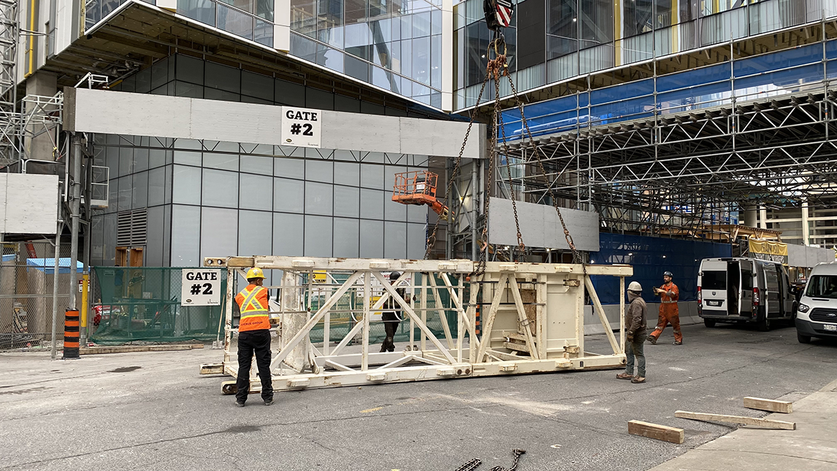 On a city street a construction worker stands next to a large rectangular structure made of white painted metal. The structure is the same height as the man