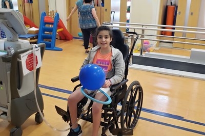 Child seated in a wheelchair connected to a large machine.